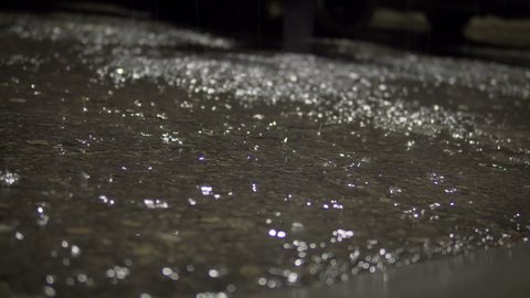 Large drops of rain fall on wet asphalt road in the night city, cinematic background loop with selective focus