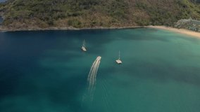 White yacht and catamaran anchored in blue water near a paradise tropical island. Self-isolation on boat. Travel business is recovering from the coronavirus pandemic. Drone video top bird eye view.