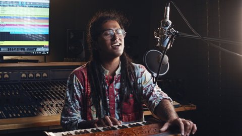 Indian people. Creative world. Hindi man playing harmonium in the sound studio. A long hair brunette male person in a traditional shirt plays meditation music.