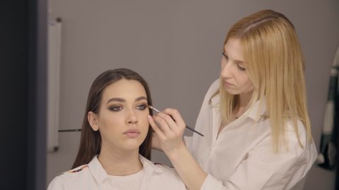 Female artist applying eye shadow with a makeup brush. Professional MUA works in the studio preparing a model for a fashion show. High quality 4k footage