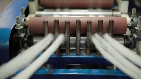 Zoomed in shot of a spinning machine, inside a wool production factory, as its multiple wheels are going at a rapid speed with the wool