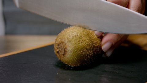 Female hands cut kiwi fruit in half. Macro shot, 150 fps, slow motion. 