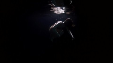 corpse of sunken woman is floating in dark depth, underwater shot of female figure in sea or river