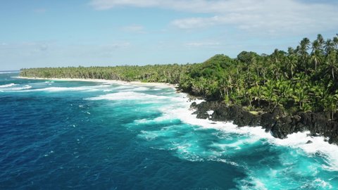 Calm view of ocean waves crushing over rocky shore. Turquoise water, rocks and palm trees. Tropical coast, siargao island, Philippines. Aerial 4k