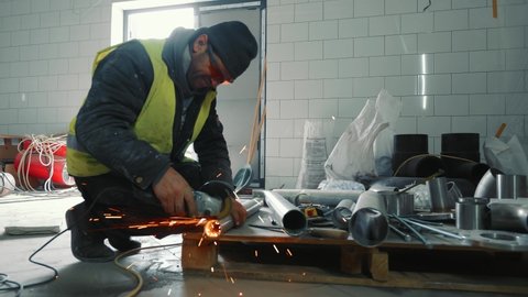 Male locksmith working in production. A man cuts a metal pipe with his hand without protection. Sparks flying off cutting a metal pipe.