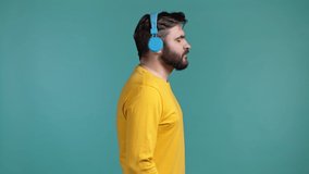 Handsome man with beard listening to music with wireless headphones, guy having fun, dancing in studio on blue background. Dance, radio concept.