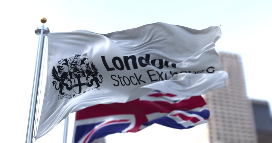 London, UK, April 2021: The London Stock Exchange flag flapping in the wind along with the UK flag blurred in the background. London Stock Exchange is a stock exchange in the City of London, England