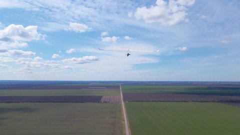 Hang glider wing soars above sunny green fields