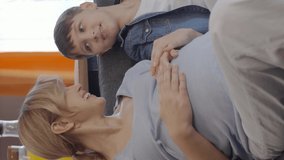 A little boy loves his pregnant mother's tummy and chats.Little boy touching abdomen of his pregnant mother. Mother child, brotherly love.Video for the vertical story.