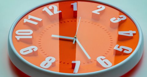 Time lapse on a modern orange wall clock.  Wall clock show the running time. Close up to a wall clock, with running time pointer. Sun and sky reflecting in the watch during the time passing by