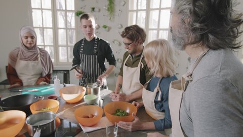 Medium shot of Caucasian adult man attending cooking class with small group of people learning to cook poached egg from young male chef giving him cooking equipment and explaining cooking techniques