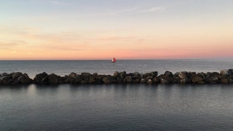 Sailing boat, red spinnaker, calm mediterranean sea at sunset