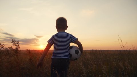 Childhood dream. boy holding soccer ball run in the park silhouette. happy family kid dream concept. kid boy run on the field silhouette at sunset carries a soccer ball fun. baby winner