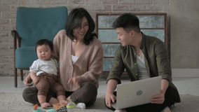 Happy young family with a baby in a cozy house inside. An Asian father turns on a laptop video call with his grandparents. Happy emotions from communication with your grandson via video chat.