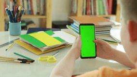 An elementary school student uses online videos to learn. Phone with Green Screen and Chroma Key in the hands of a Primary school student. Schoolboy Scroll Up Cellphone by Finger. 