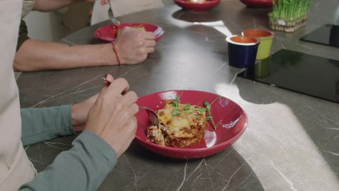 From-above close up with slowmo of unrecognizable people eating delicious self-cooked lasagna during cooking master class