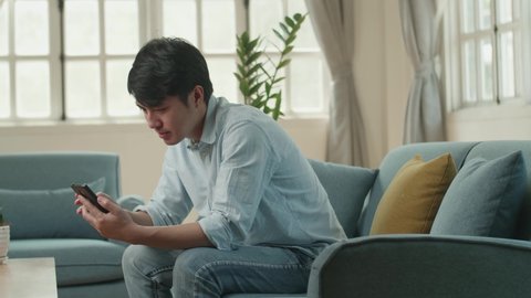 Asian Male Using Smartphone And Celebrates In Living Room