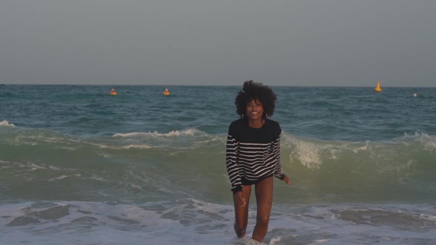 Young black woman having fun in the waves running and smiling
