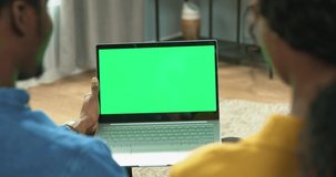Young African American couple sitting at home on couch and watching videos online on laptop. Green screen.