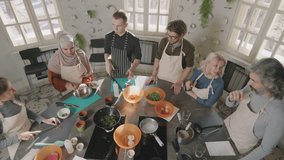 Slow-motion top-view shot of small diverse group of people having good time attending cooking class with chef in modern culinary school - Powered by Shutterstock - Get 15% off with code: PIKWIZARD15