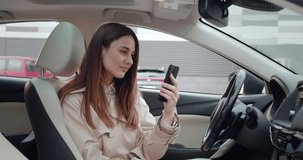 Portrait of young woman talking by videoconference using smartphone while sitting in the car. Female entrepreneur greets by video chat, remote work concept.