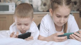 Smiling cute preschool kids sit watch funny videos on smartphone gadget. Friendship, care, support. Happy small brother and sister siblings relax on sofa at home. The concept is always together.