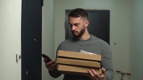 Delivery man standing at door of customer apartment with boxes of hot pizza and calling client on phone. Courier wearing casual clothing has problem with delivery of order. Shooting in slow motion.