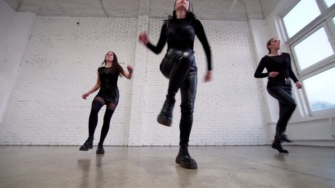 View from below of three attractive women in black costumes performing modern shuffle dance in the studio