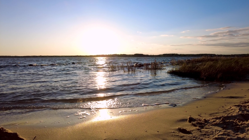 View of the sunset across Chesapeake bay as seen from the town of Oxford on the coast of Tred Avon River leading to the bay. There are sand grasses on the beach. Sunlight reflects from water.