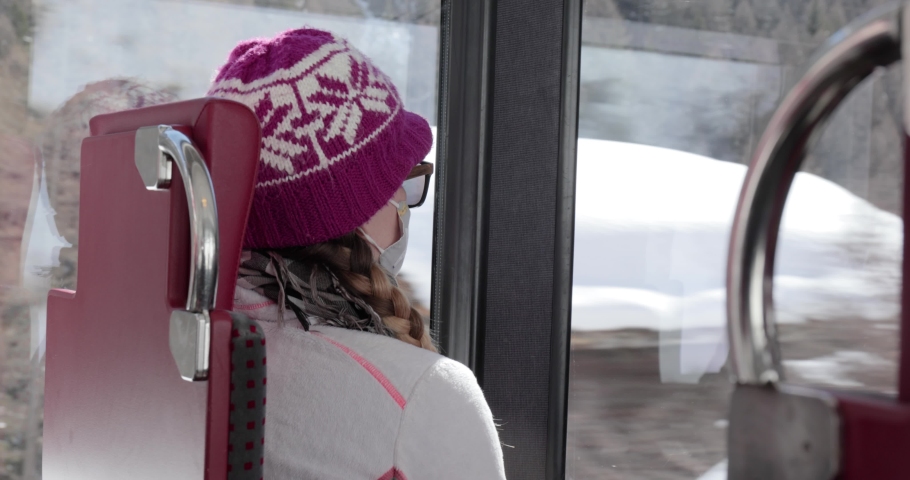 Woman traveling on a swiss train in the snowy alpine mountains, wearing mask during coronavirus pandemic