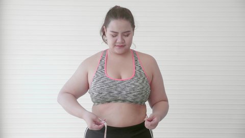 Young asian woman overweight measuring waistline with tape and feeling worried and displeased at home, female fat dieting failure, plus size, emotion and expression with frustration, health care.