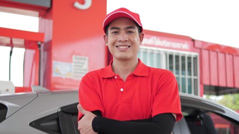 Positive filling station Asian employee keeping arms crossed and looking at camera while standing near pump and modern vehicle at gas station service, Slow motion