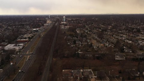 An aerial view of an empty railroad tracks. Residential homes are on the right, a highway, businesses on the left. The drone camera dolly in over the tracks as it flurries on Long Island.