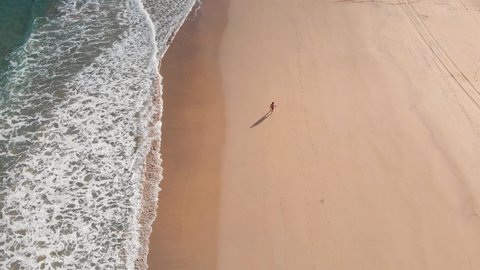 One person walking alone on golden beach at Porto Santo island, Portugal. Aerial tilt-up