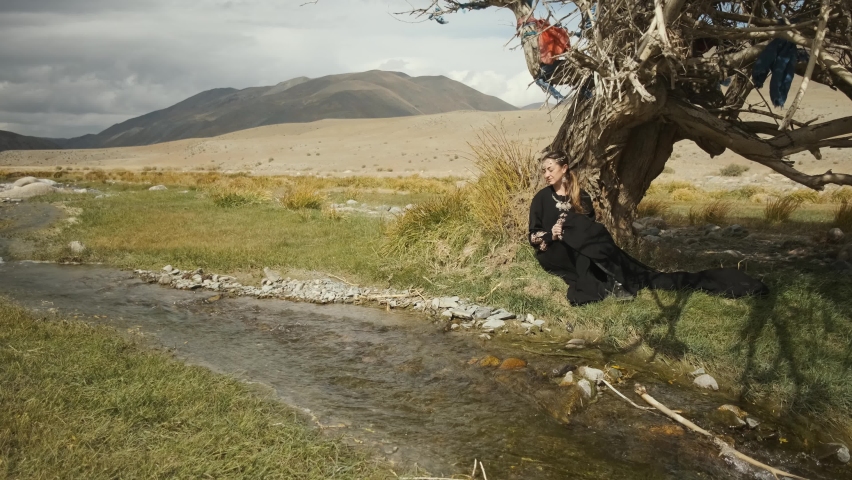 Caucasian girl on background of mountains and blue sky,black dress fluttering in wind