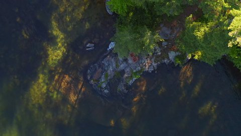 Aerial top down view of two Adirondack chairs sitting on a rock formation near a lake in Ontario, Canada filmed by drone moving up slowly showing more of the surrounding cottage country