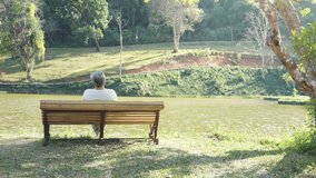 4K Rear view of loneliness Asian senior man sitting alone on bench in the park. Elderly retired male relax and enjoy outdoor leisure activity in sunny day. Health care and illness recovery concept - Powered by Shutterstock - Get 15% off with code: PIKWIZARD15