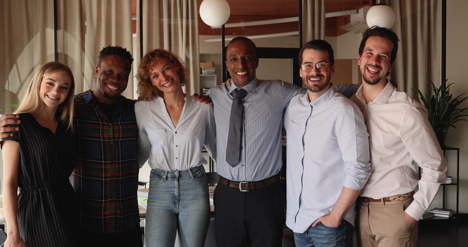 Happy motivated friendly diverse multiracial colleagues, embracing shoulders, posing in modern office room. Group of smiling mixed race employees demonstrating strong team spirit, looking at camera. Royalty-Free Stock Footage #1071051430