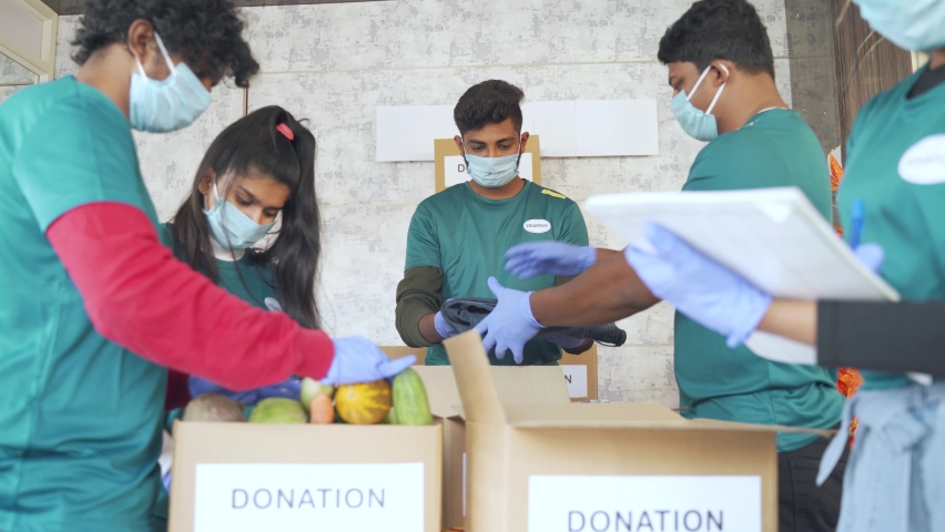 Group of volunteers busy working by arranging vegetables and clothes on donation boxes and noting down during coronavirus covid-19 pandemic lockdown for needy people. Royalty-Free Stock Footage #1071052138