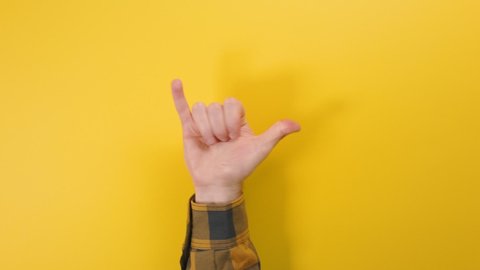 A man's hand appears from below and makes a shaka gesture. Yellow background. Concept of positive gestures