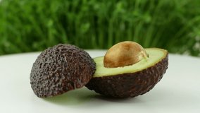 Avocado rotates on a green grass background. 4K video close-up of wholesome and healthy food. Avocado with a bone in a cut, rotating in slow motion.
