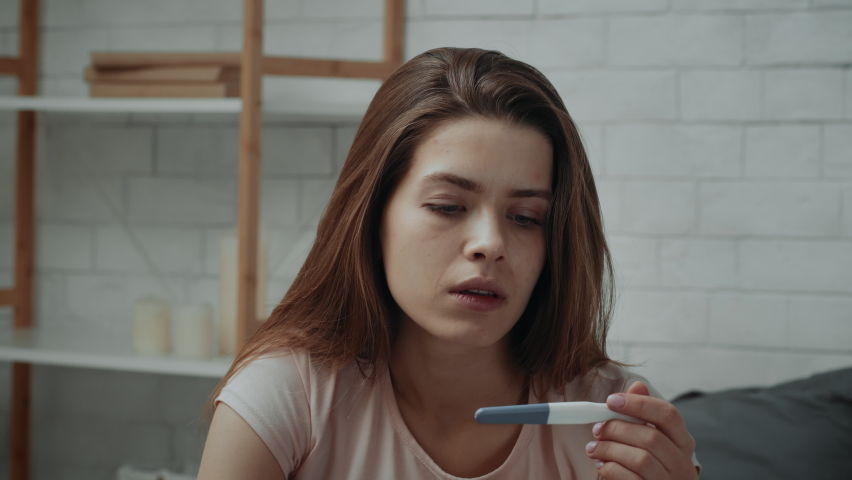 Unplanned Pregnancy. Shocked Pregnant Young Lady Looking At Positive Pregnancy Test Result Sitting In Dark Bedroom At Home. Unwanted Pregnancies Reaction Concept. Zoom In | Shutterstock HD Video #1071066754