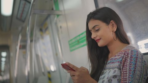 Close shot of a young attractive Indian female in traditional salwar kurta sitting on a moving city metro train and typing a text message on a mobile phone 