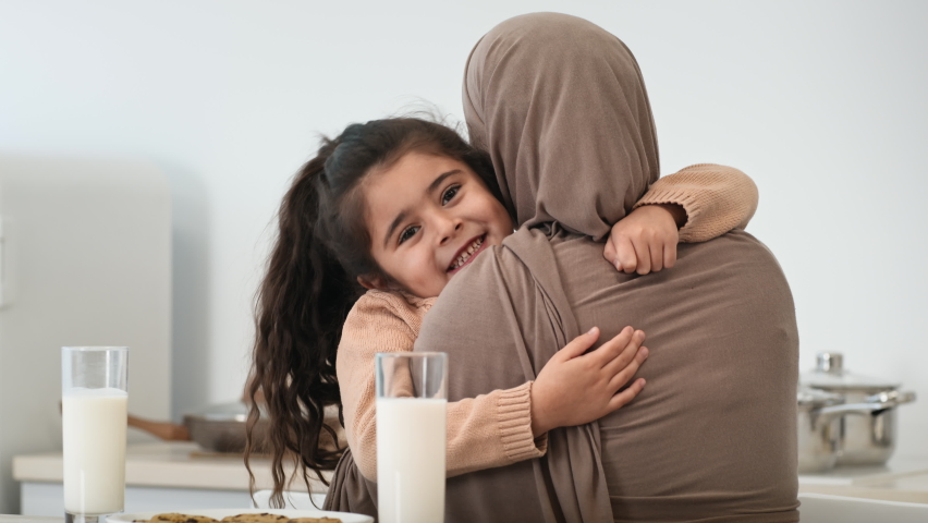 Muslim Mom In Hijab Hugging Little Daughter Sitting In Kitchen At Home Having Lunch Together. Cute Kid Girl Embracing Her Mommy. Modern Arabic Family Lifestyle, Mother's Love Concept Royalty-Free Stock Footage #1071070429