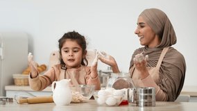 Joyful Muslim Mom In Hijab And Little Daughter Clapping Hands Having Fun With Flour While Baking Pastry In Kitchen At Home. Young Arabic Mother And Her Kid Girl Enjoying Cooking Cookies Together