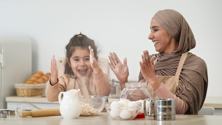 Joyful Muslim Mom In Hijab And Little Daughter Clapping Hands Having Fun With Flour While Baking Pastry In Kitchen At Home. Young Arabic Mother And Her Kid Girl Enjoying Cooking Cookies Together | Shutterstock HD Video #1071070432