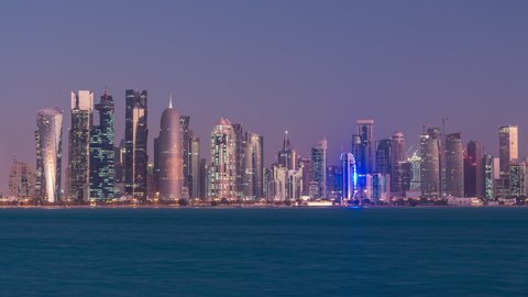 Skyline of the arabian city of Doha night to day transition timelapse in Qatar, captured in the very early morning before sunrise with illuminated skyscrapers. View from Corniche Promenade