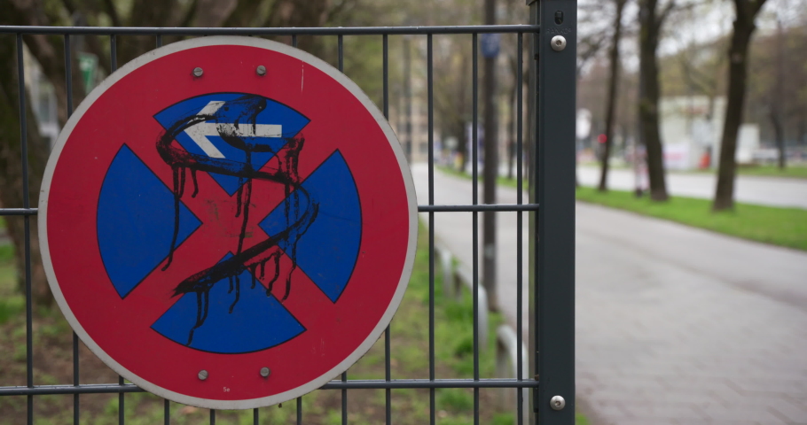 Road sign absolute no stopping with graffiti attached to a fence in front of a blurred background with cyclists and postmen on bicycle