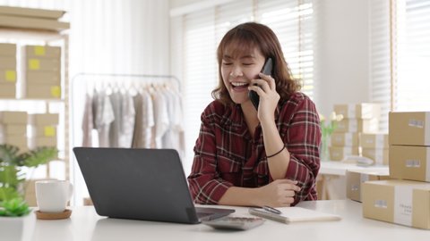 Asian entreprenuer woman online seller confirming orders from customer on the phone. Online web store owner taking order on phone, texting message online. Phone call receive from customer