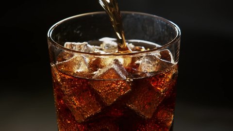 Pouring Cola with ice cubes. Cola with Ice and bubbles in glass. Soda closeup. Food background. Rotate glass of Cola. Slow motion 4K video footage. Macro Shot. Close-up.